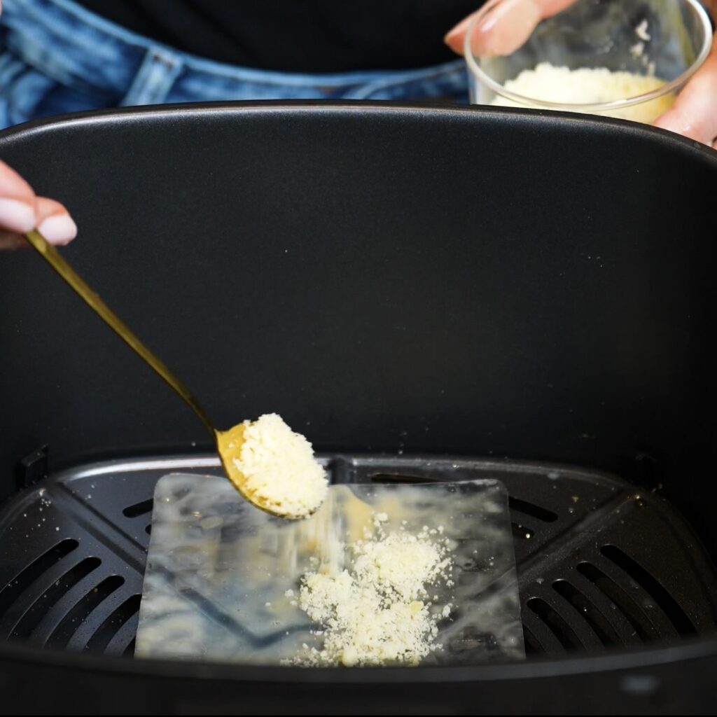 Sprinkling grated Parmesan over a rice paper square in the air fryer basket.