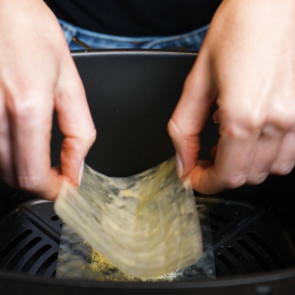 Adding a second rice paper square over the Parmesan layer in the air fryer basket.