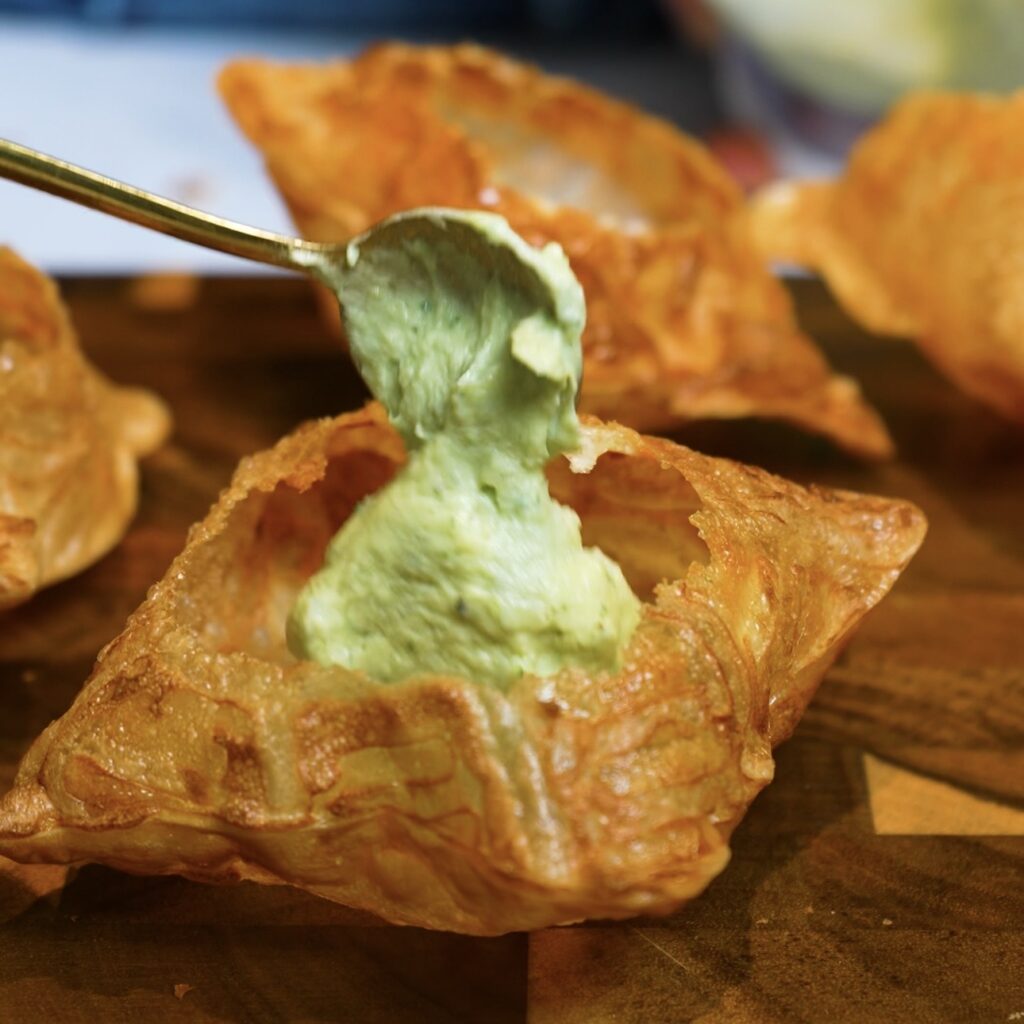 Spooning creamy avocado and cottage cheese filling into a crispy rice paper tart case.