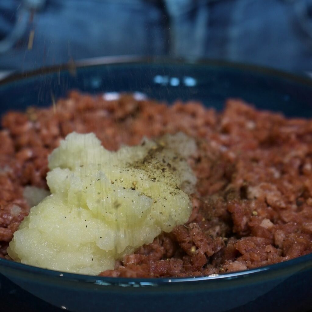 Grated onion, salt and pepper added to minced beef for Azerbaijani Qutab