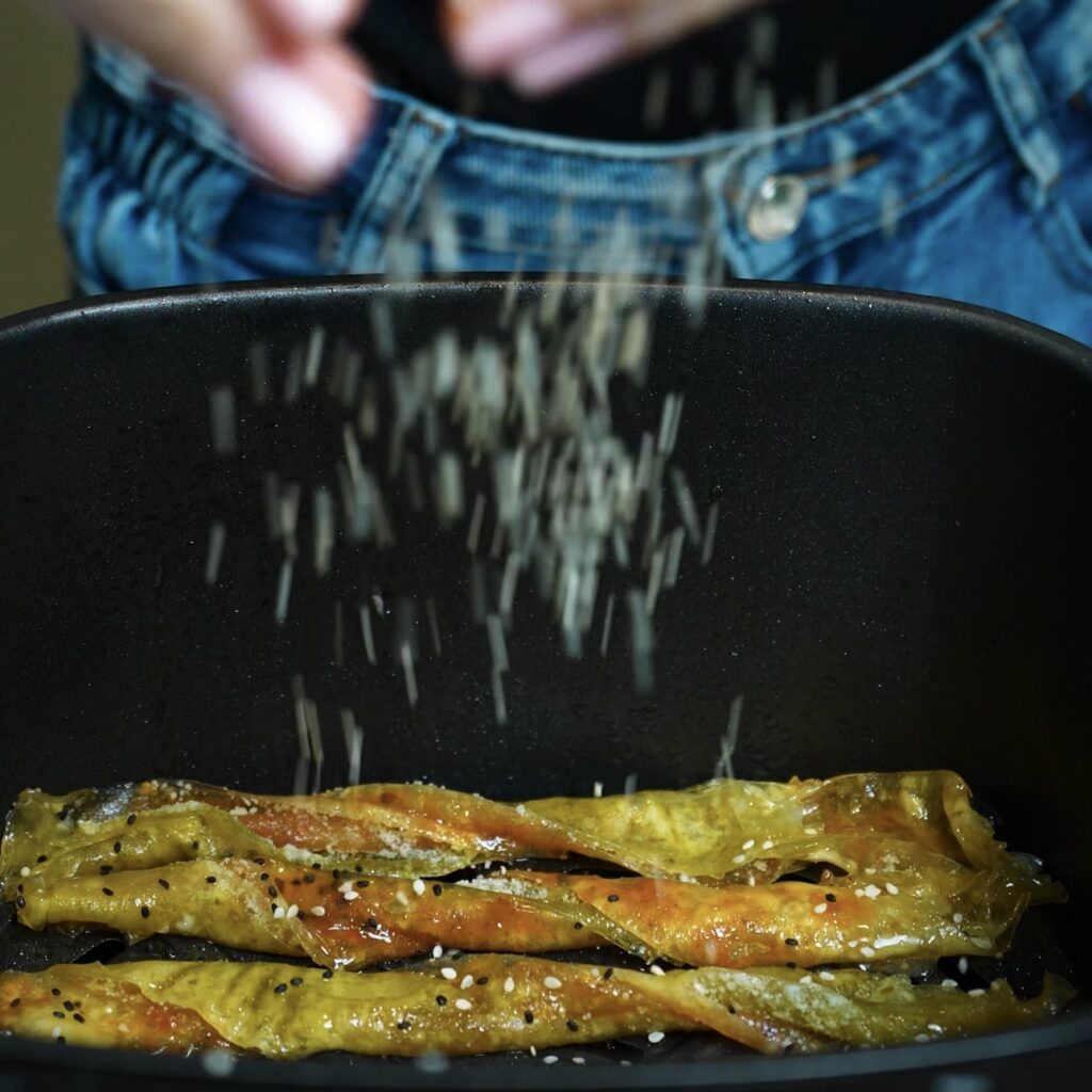 Sprinkling sesame seeds over Pesto Parmesan Rice Paper Twists before air frying