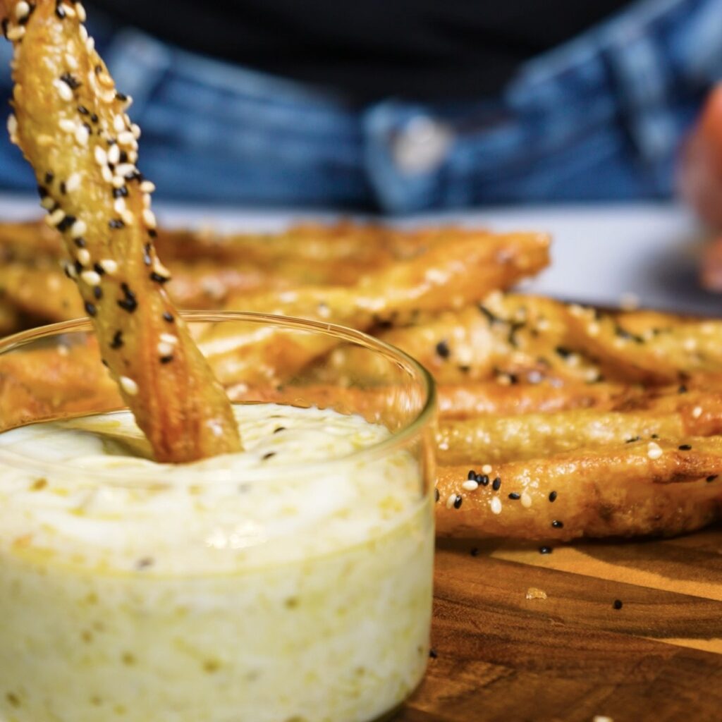 Dipping a Pesto Parmesan Rice Paper Twist into garlic yogurt pesto sauce