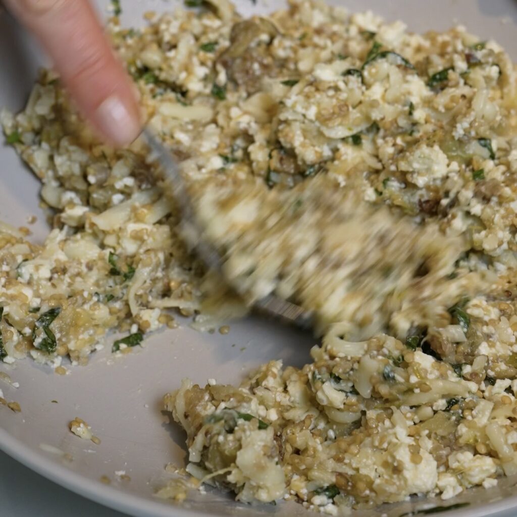 Mixing roasted aubergine, feta, mozzarella, basil and garlic in a bowl