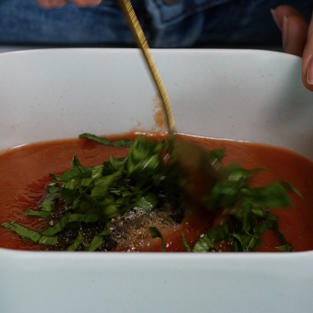 Mixing passata with basil, coriander, salt, pepper and sugar in a square baking dish.