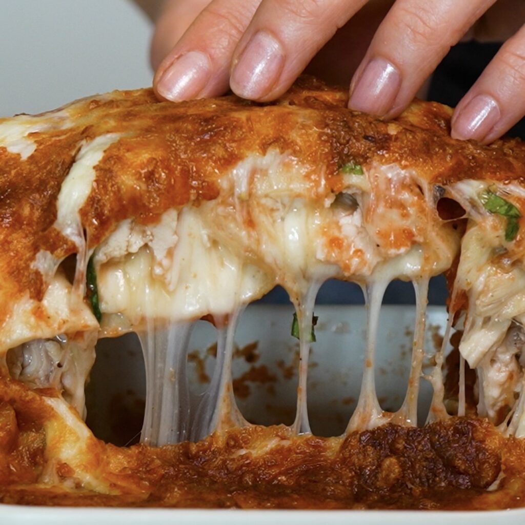 Lifting half of 20-Minute Air Fryer Cheesy Chicken Tortilla Rolls from the baking dish with a melted cheese pull.