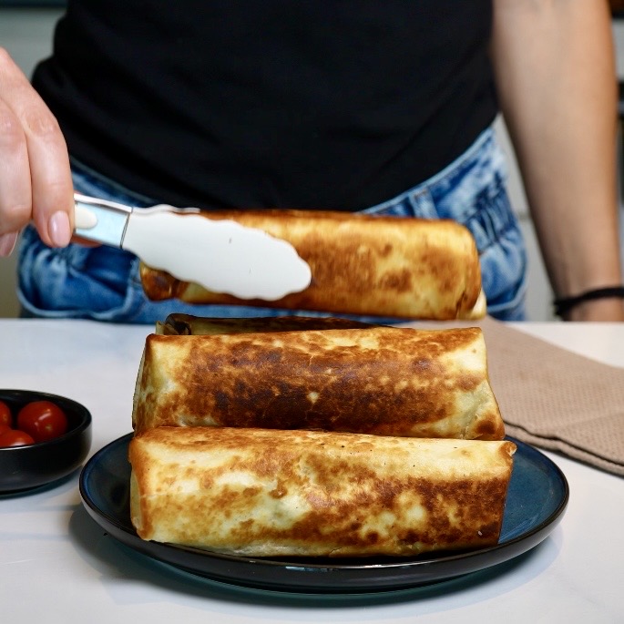 Freshly fried Cheeseburger Tortilla Roll being placed alongside other golden, crispy tortilla rolls.