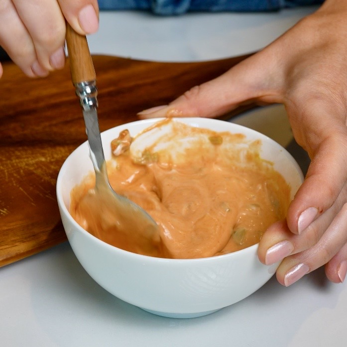 Mixing ketchup, mayonnaise, mustard and finely chopped cornichons in a small bowl to make burger sauce for Cheeseburger Tortilla Rolls.