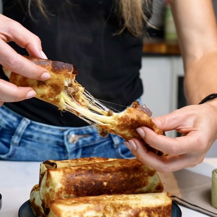 Breaking apart a crispy Cheeseburger Tortilla Roll to reveal the juicy beef filling and stretchy melted cheese pull.