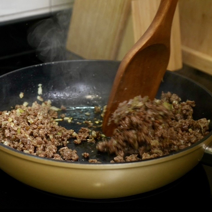 Minced beef and finely chopped onion cooking together in a frying pan for Cheeseburger Tortilla Rolls.