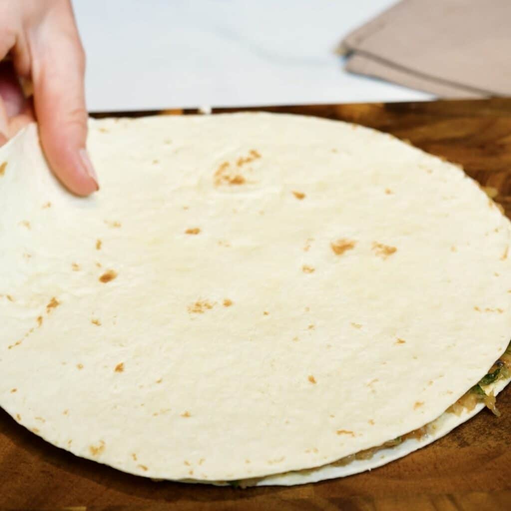 A second flour tortilla placed over the seasoned chicken mince filling, forming a layered tortilla sandwich.