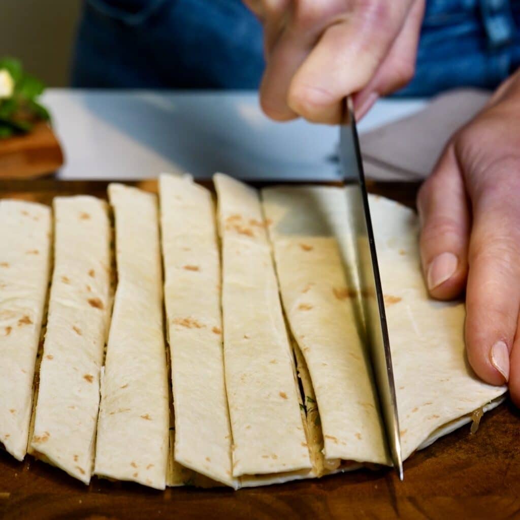 Layered tortillas with chicken filling being cut into strips on a work surface.