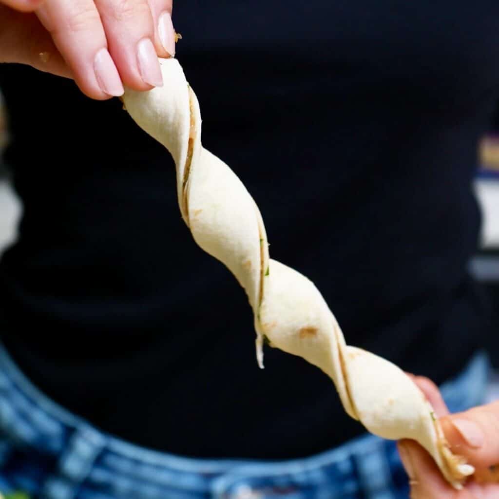 A strip of layered tortilla with chicken filling being twisted into shape by hand.