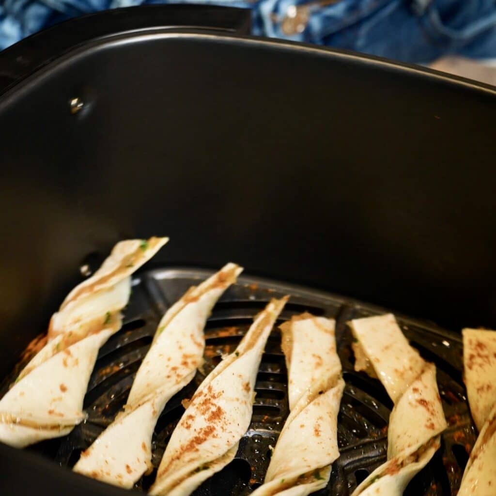 Twisted tortilla strips filled with seasoned chicken mince arranged in a single layer inside an air fryer basket.