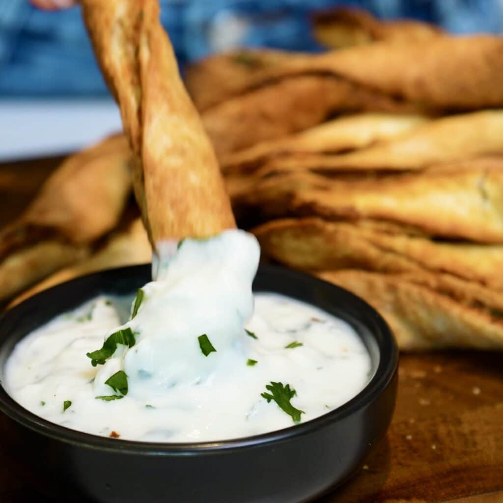 Crispy golden chicken tortilla twist being dipped into a creamy garlic yoghurt sauce.