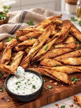 Crispy chicken tortilla twists served on a wooden board with a bowl of garlic yoghurt dip.