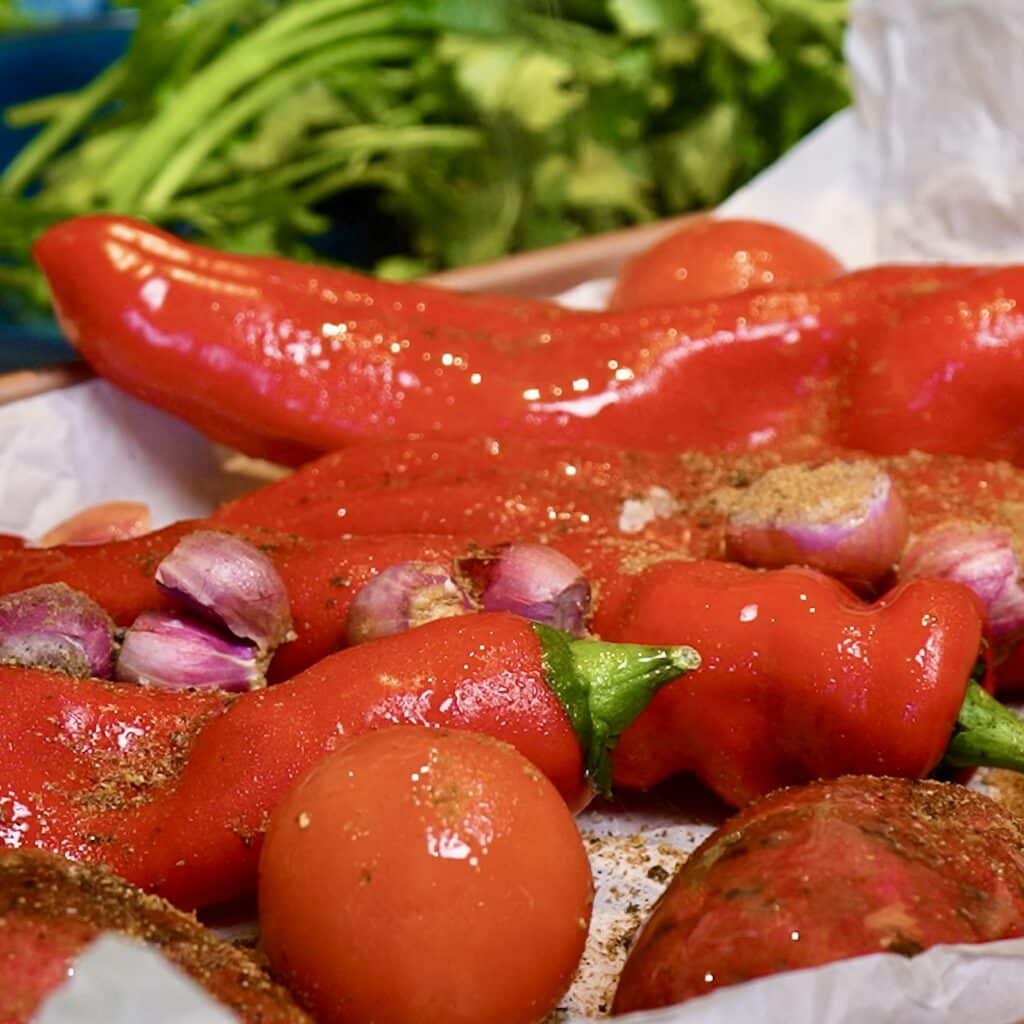 Red peppers, tomatoes, sweet potato, garlic and shallots on a baking tray before roasting.
