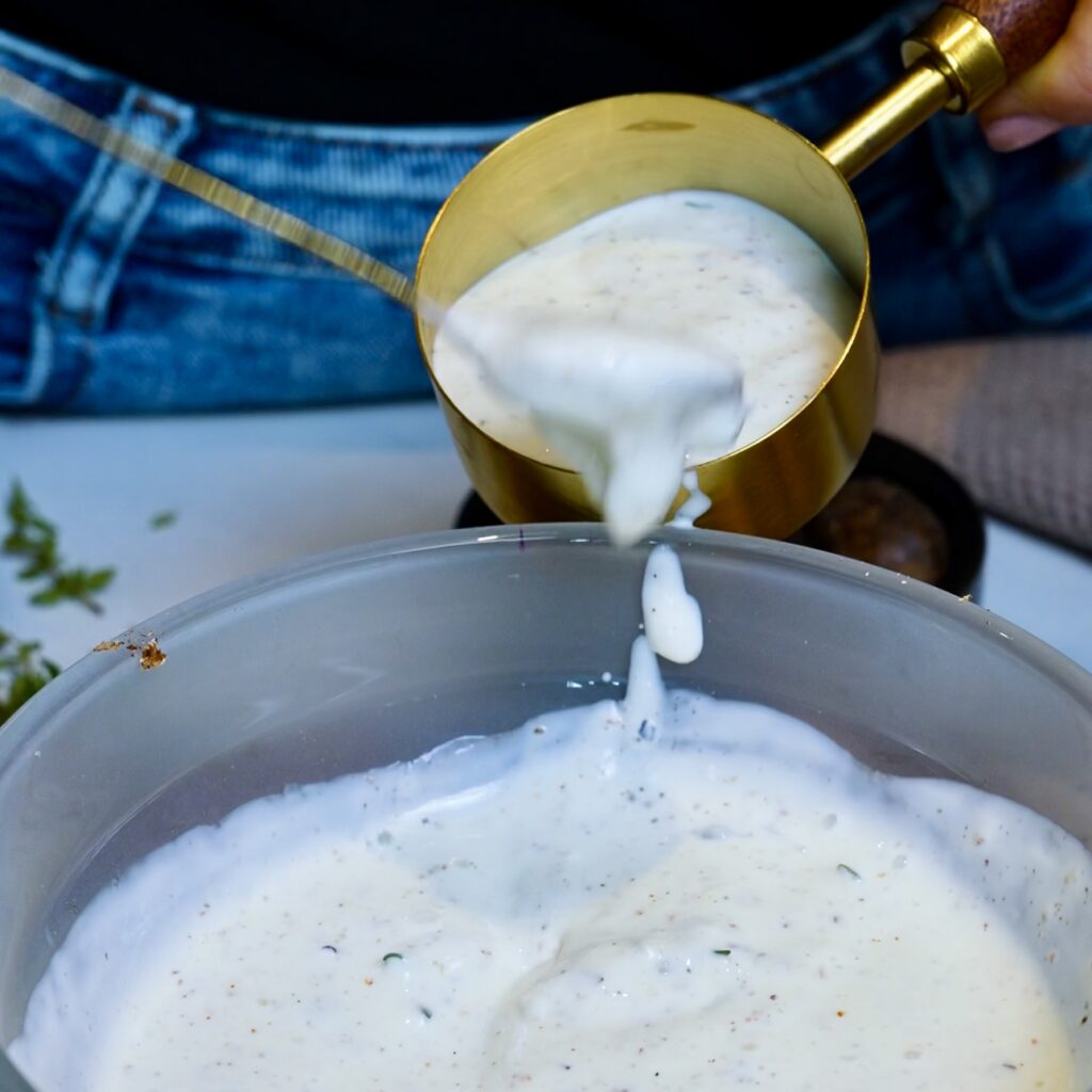 Scooping seasoned cooking cream from the baking dish into a measuring cup.