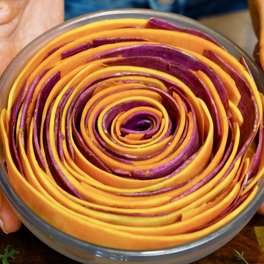Assembled gratin with butternut squash and purple sweet potato ribbons arranged in a beautiful swirl pattern in the baking dish.