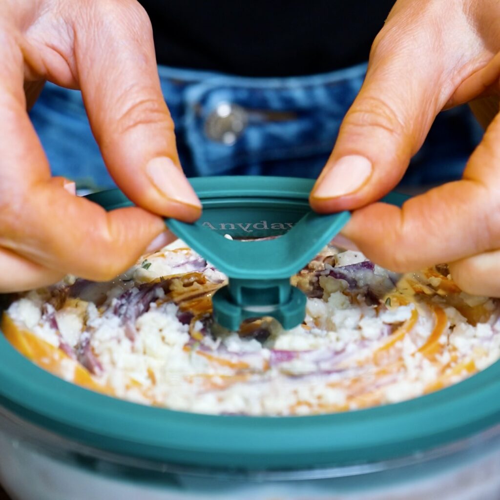 Gratin covered with a microwave-safe lid, with the ventilation knob lifted to release steam.