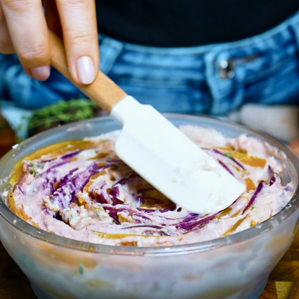 Spreading the risen cream evenly over the butternut squash and purple sweet potato gratin after microwaving.