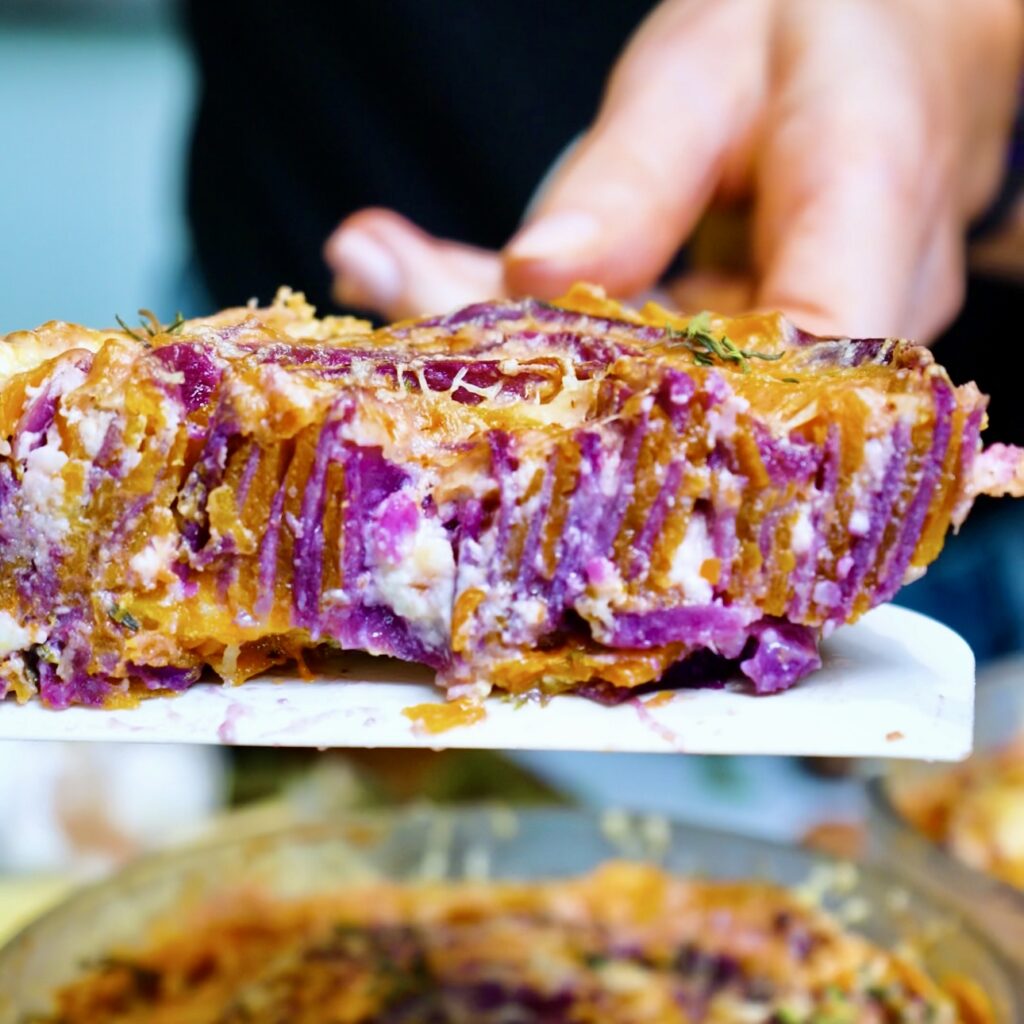Butternut squash and purple sweet potato gratin cut in half to reveal its creamy, colourful layers.